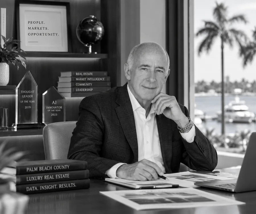 Black-and-white portrait of David Abernathy seated at a desk, with awards, books and a waterfront setting behind him