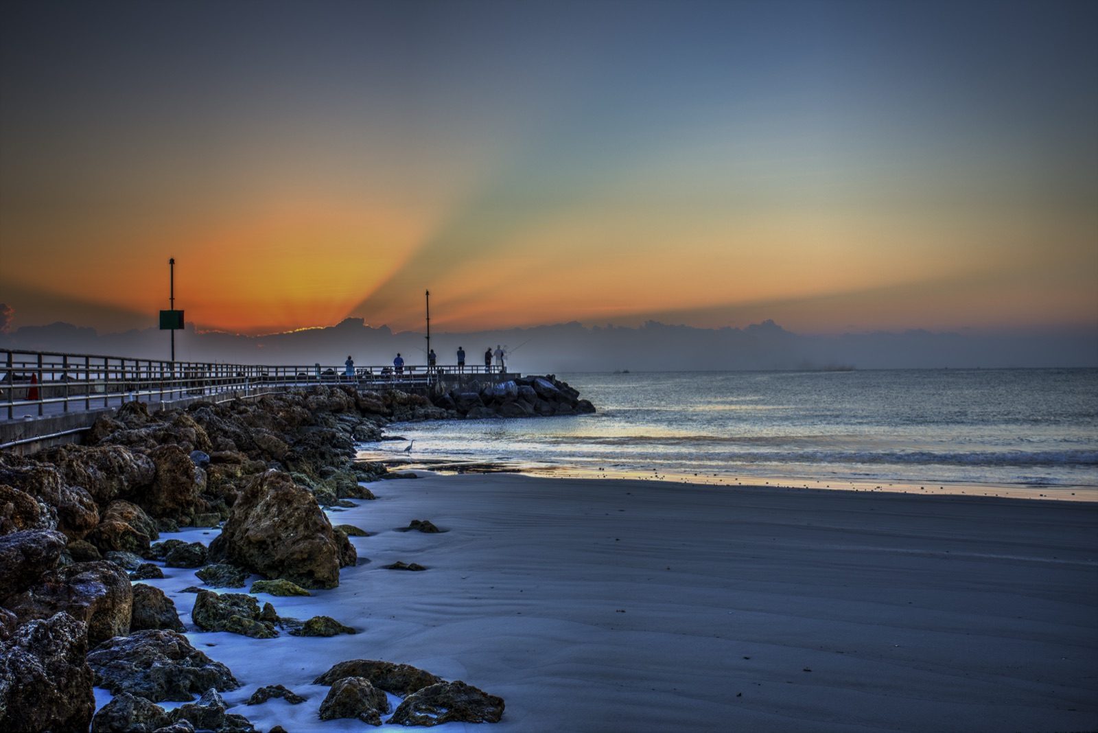 Sunrise over the Jupiter Inlet jetty with fishermen along the rocks.